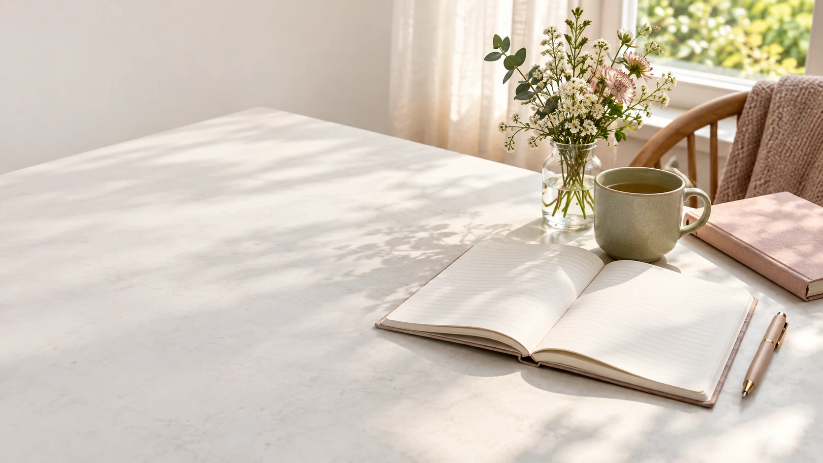 An open journal, sage tea mug, blush notebook, and fresh flowers in soft window light